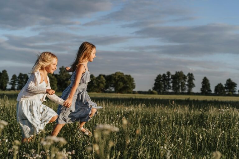 Two happy young sisters running hand in hand through a sunlit meadow.